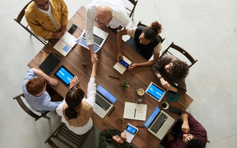 Top view of a diverse team collaborating in an office setting with laptops and tablets, promoting cooperation.